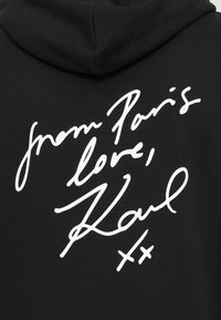 Felpa nera con cappuccio caratterizzata da testo scritto a mano bianco sulla schiena che recita: "da Parigi, amore, Karl." Tessuto morbido e vestibilità comoda.