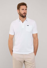 Biała koszulka polo wykonana z bawełny, z kołnierzykiem, trzema guzikami i kieszonką na lewej piersi. Krótkie rękawy oraz dopasowany krój.