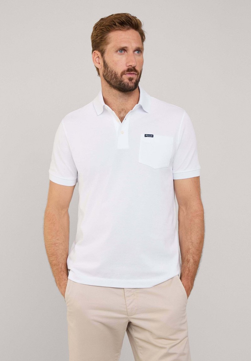 Camisa polo blanca con cuello, mangas cortas y un bolsillo en el pecho izquierdo con una etiqueta de marca. Textura suave y diseño clásico.