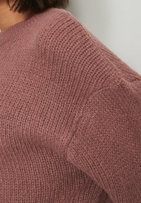 Sweter dziany w kolorze przygaszonego różu o fakturowanej powierzchni. Charakteryzuje się luźnym fasonem, prążkowanym dekoltem oraz opuszczonymi ramionami dla większego komfortu.