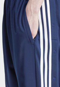Pantalones deportivos en navy fabricados en un tejido suave, que cuentan con un bolsillo lateral y tres franjas verticales blancas a lo largo del costado, con cierres a presión.