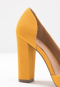 Chaussure à talons hauts jaunes en matériau texturé avec un motif reptilien, dotée d'un large talon carré et d'un bout pointu.