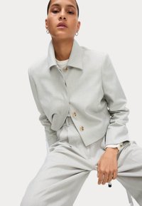 Ljust grå kort blazer med spetsig krage, knappstängning fram, sidofickor och textil med struktur, i kombination med matchande byxor.