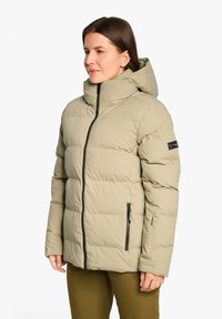 Giacca a vento imbottita di un verde oliva chiaro con cappuccio, chiusura con zip e dettagli neri; presenta cuciture orizzontali e tasche laterali.