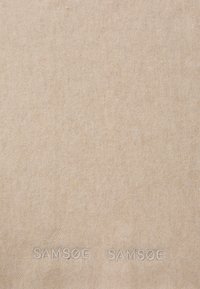 Beige stof met een zachte textuur, voorzien van een subtiel geweven patroon. Geborduurde "SAMSØE" branding verschijnt onderaan in bijpassende kleur.