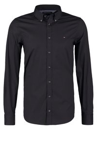 Camisa negra de manga larga con botones y un pequeño logotipo rojo, blanco y azul en el lado izquierdo del pecho, y cuello abotonado.