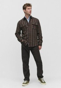 Flanellhemd mit rot, grün und gelb kariertem Muster, zwei Brusttaschen, Knopfverschluss, lange Ärmel, über einem blau gestreiften Hemd getragen.