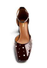 Zapato de charol marrón de tacón alto con correa al tobillo, que presenta tachuelas metálicas y una punta afilada. Superficie suave y brillante con un diseño minimalista.