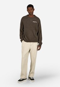 Brązowy puszysty sweter z logo "pagador", połączony z kremowymi spodniami w kratę. Czarno-białe sneakersy dopełniają stylizację.