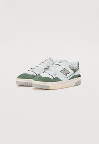 Zapatillas verdes y blancas que presentan materiales de ante y malla, una suela de goma gruesa y el logo "N" en gris en el costado.