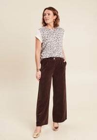 Leopardprint shirt met korte mouwen, gecombineerd met brede bruine corduroy broeken en gouden hakken. Textuur van de stof en knoopdetails zichtbaar.