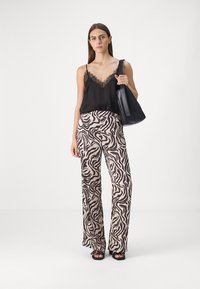 Black lace-trimmed camisole paired with beige zebra-print wide-leg pants. Model carries a black tote bag and wears black sandals.