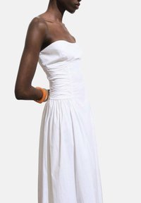 Witte strapless jurk met geplooide details, een getailleerde korsage en een vloeiende rok. Licht van textuur met een simpel, elegant ontwerp.