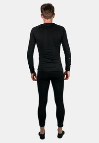 Schwarzes athletisches Langarmshirt und Leggings aus strukturiertem Material, mit tailliertem Design und nahtloser Verarbeitung. Ansicht von hinten.
