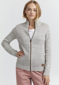 Gaiši pelēks zip-up kardigāns no teksturētas adītas auduma, ar augstu apkakli un ribotām piedurknēm, rotāts ar mazu ādas logotipa etiķeti.