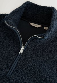 Marine fleece pullover med lynlås i kraven, herunder tekstureret, blødt materiale og sølv lynlåsdetalje. Mærket viser størrelse medium.