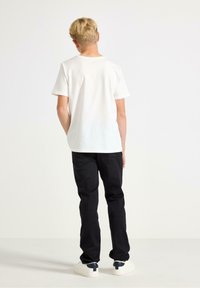 Vit bomull t-shirt och svarta denimbyxor bärs tillsammans. Byxorna är åtsittande med en klassisk fem-fickorsdesign. Vita sneakers fulländar looken.