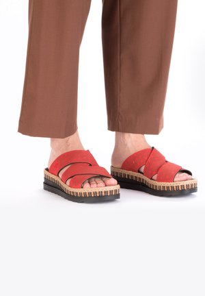 Sandales rouges à semelle plate avec des lanières croisées, en matériau texturé, et une semelle en liège et en caoutchouc noir présentant un design en couches.