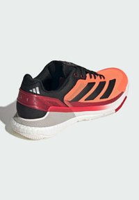 Sportovní obuv s jasně oranžovým a černým designem, síťovaným svrškem, třemi černými pruhy, červenými akcenty a strukturovanou bílou podrážkou.