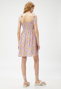 Vestido floral con un cuerpo fruncido, tirantes ajustables y una paleta de colores pastel que presenta flores amarillas, rosas y moradas.
