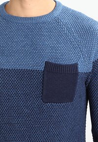 Pull tricoté en dégradé de bleu avec des motifs texturés ; comporte une poche plaquée bleu foncé ; encolure ronde ; poignets côtelés.