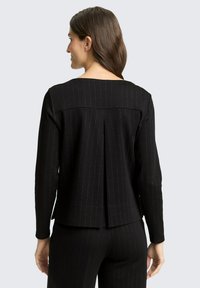 Czarny top z długim rękawem i pionowymi paskami, z kwadratowym karczkiem z tyłu i detalem plisowania. Gładka tkanina z delikatnym połyskiem.