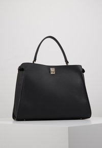 Sac à main en cuir noir avec une forme structurée, une texture grainée et un fermoir métallique. Dispose de poignées courtes en cuir et d'un design minimaliste.