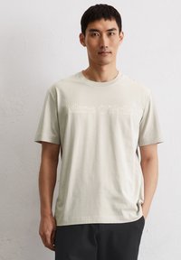 Lichtbeige korteblauwe t-shirt met een ronde hals, met een subtiele "Marc O’Polo" logo in een textuurdesign over de borst.