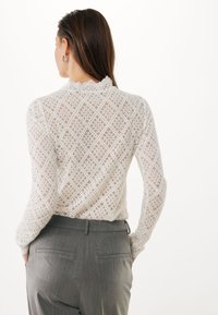 Top bianco in pizzo lavorato a maglia con motivo a diamante, scollatura rotonda e maniche lunghe. Abbinato a pantaloni grigi su misura con tasche posteriori.