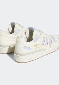 Zapatillas de piel blanca con acentos en azul claro, rayas rojas y marca en dorado. Presentan un collar acolchado y una suela texturizada.
