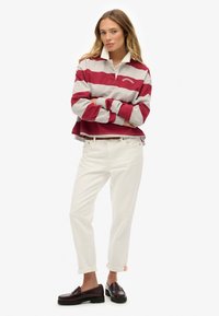 Rød og grå stribet pullover med hvid krave, parret med hvide jeans med opsmøg og mørke loafers. Casual, løs pasform design.