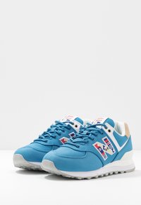 Baskets en tissu bleu avec accents blancs et semelles en caoutchouc gris, arborant un logo coloré brodé sur le côté et une tige texturée.