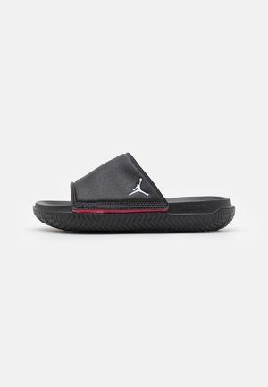 Czarna sandałka typu slide z teksturowaną podeszwą, czerwonym obszyciem i białym logo Jumpman na szerokim pasku na górze stopy.