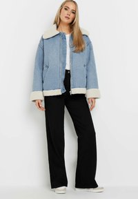 Blå denimjacka med vit fuskpälskrage och manschetter, dragkedja fram, sidofickor, kombinerad med svarta vida byxor och sneakers.