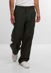 Cargo-Hosen aus dunkelgrünem Baumwollstoff, mit einem lässigen Schnitt, seitlichen Taschen und einer Knopfverschluss. Tragen Sie dazu weiße Sneakers.