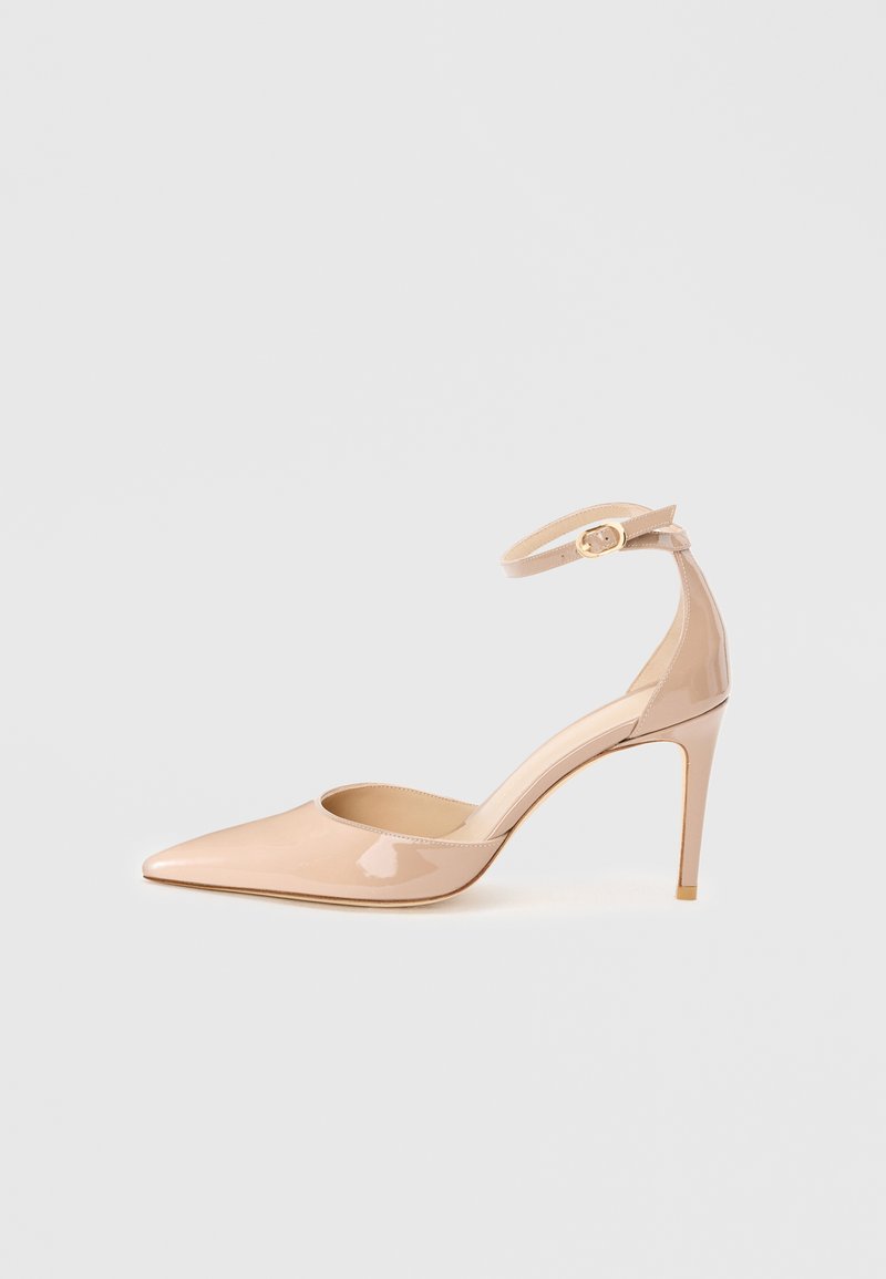 Chaussure à talon haut en cuir verni nude à bout pointu avec bride à la cheville et boucle dorée, vue de profil sur un fond uni.
