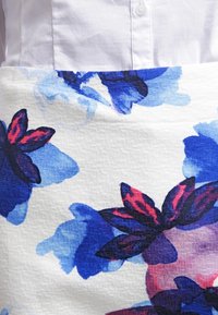 Floraler Rock aus strukturiertem weißem Stoff mit blauen und roten Blumenmustern. Verfügt über einen glatten Bund und dezente horizontale Streifen in der Struktur.