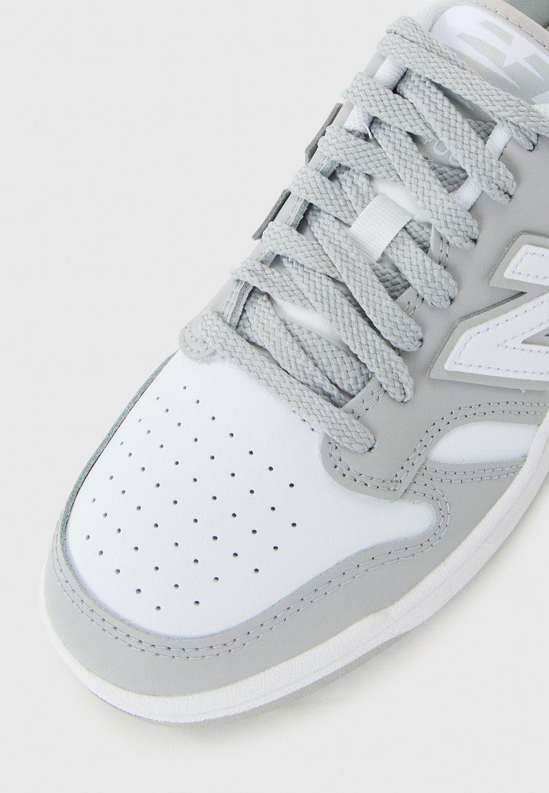 White and gray sneaker with perforated toe, textured laces, and a visible side logo on a plain white background.