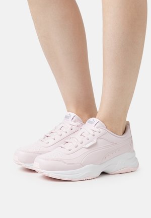 Zapatillas deportivas de color rosa claro con parte superior de piel suave, media suela blanca, perforaciones para transpirabilidad y cordones para un ajuste seguro.