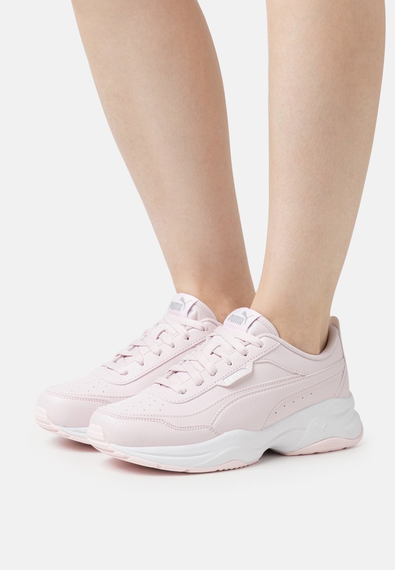 Baskets de sport rose clair avec une tige en cuir lisse, une semelle intermédiaire blanche, des perforations pour la respirabilité et des lacets pour un maintien sécurisé.