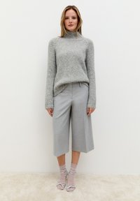 Grijze gebreide trui met een hoge halslijn, gecombineerd met grijze culottes. Het model draagt lichtgrijze sokken en open-toe hakken met strikken.