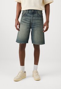 Șorturi din denim într-o nuanță de albastru estompat, cu un design drept, cinci buzunare și tiv cusut. Purtați cu adidași și șosete de culoare deschisă.