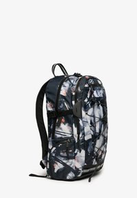 Sac à dos avec un motif abstrait bleu foncé et blanc, comprenant plusieurs compartiments zippés et un design de cordon unique à l'avant.