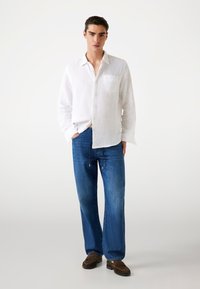 Camisa blanca de lino de botones con bolsillo, combinada con pantalones de denim azul holgados y zapatos mocasines marrones. Diseño simple y casual.