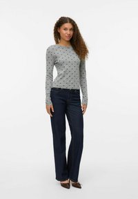 Grå långärmad topp med små hjärt-mönster, matchad med mörkblå raka jeans och bruna klackskor. Slät tygtextur.