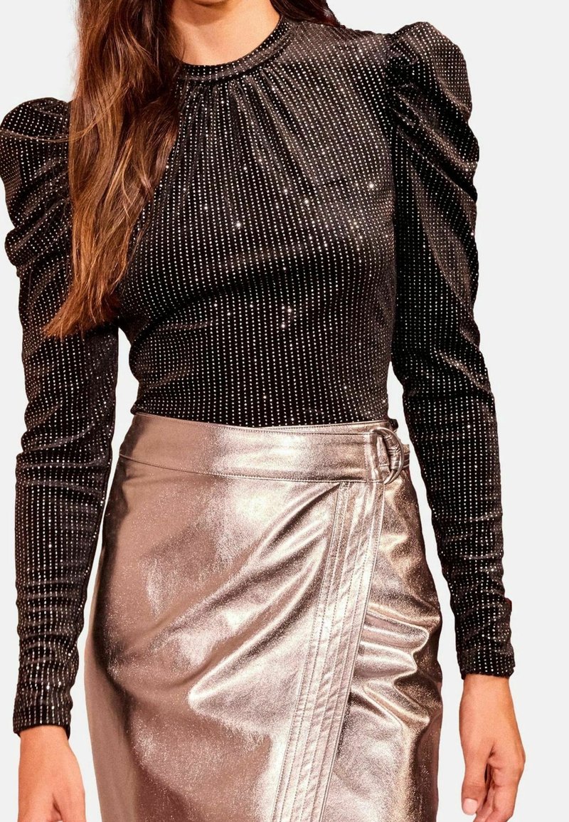 Haut noir à manches longues avec des pois argentés et des épaules bouffantes, associé à une jupe portefeuille argentée métallique taille haute avec un détail boucle.
