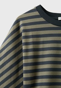 Gros plan d’un tissu avec des rayures horizontales vert olive et gris foncé, et un col rond uni gris foncé.