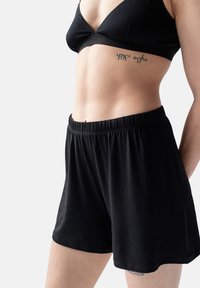 Zwarte shorts met elastische taille en een gladde textuur, met een losse pasvorm. Gecombineerd met een zwarte bralette, die een minimalistisch ontwerp toont.
