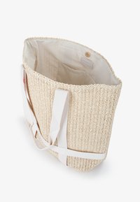 Borsa a tracolla in paglia intrecciata di un leggero color beige con manici in tessuto bianco. L'interno è foderato in modo uniforme e presenta un'etichetta decorativa con chiusura a bottone.