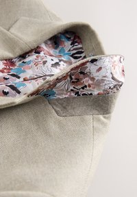 Sac en tissu beige texturé avec un rabat plié révélant une doublure à motif floral coloré à l’intérieur.